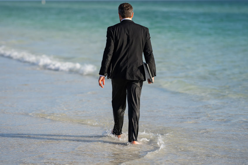 Rear view of back business man in suit in sea water at beach. Summer rest, business people concept. Business man remote on-line working. Dream for summer vacations office workers.